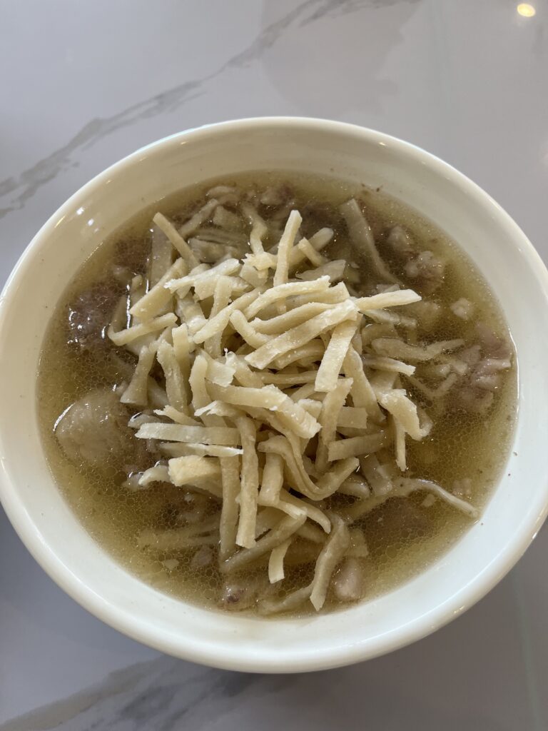 A top-down view of a bowl of Mongolian noodle soup (Guriltai Shul), featuring flat, handmade noodles in a savory meat broth.